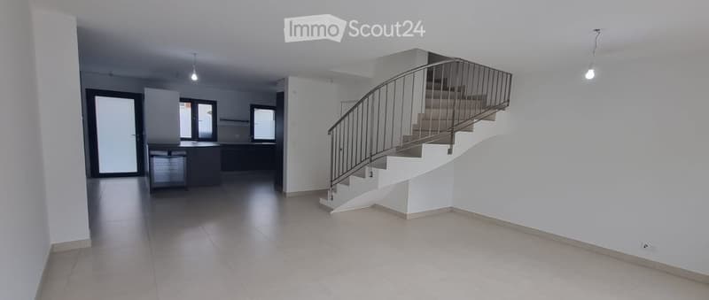 Empty room with tiled floor, white walls, and a staircase leading to an upper level. The room has large windows and a modern design.