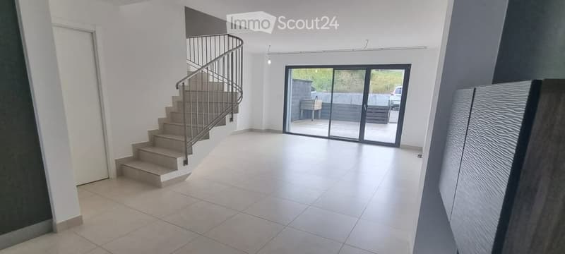 Bright, modern hallway with tiled flooring, a curved staircase with metal railing, and large glass sliding doors leading to an outdoor area.