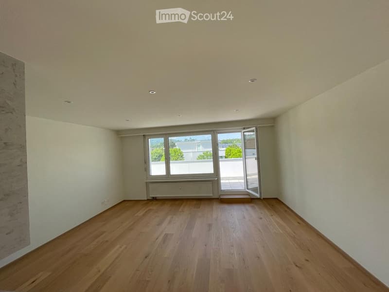 Empty room with wooden flooring, white walls, large window with view, and sliding glass door leading to a balcony.