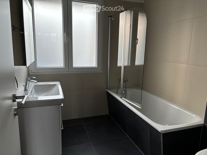 Bathroom. Modern bathroom with a white sink, chrome faucet, bathtub with glass enclosure, and large windows providing natural light.