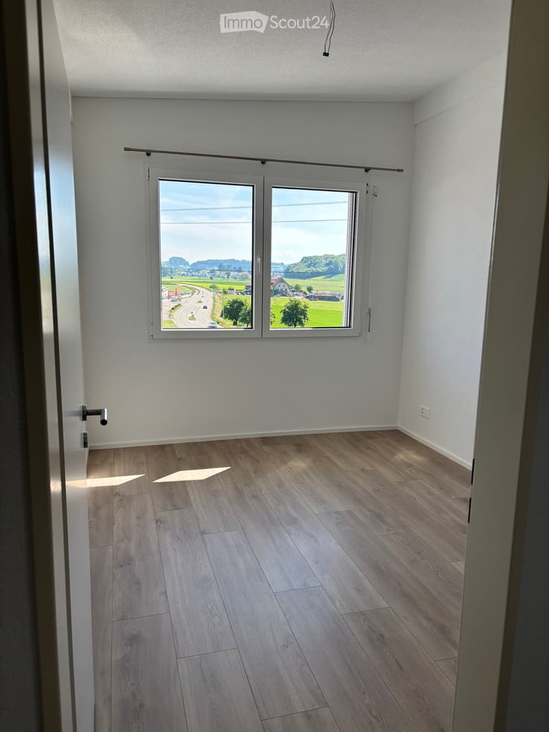 Unfurnished Room. Empty room with light wooden flooring, white walls, and large windows offering a view of a rural landscape.