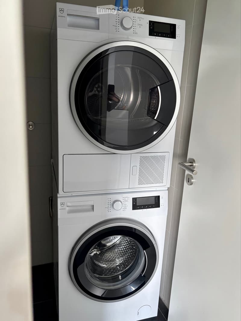 Bathroom. A modern bathroom with a stacked washing machine and dryer unit, featuring sleek white finishes and digital control panels.