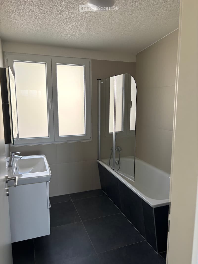 Bathroom. Modern bathroom with a white sink, chrome faucet, bathtub with glass shower enclosure, and large windows providing natural light.