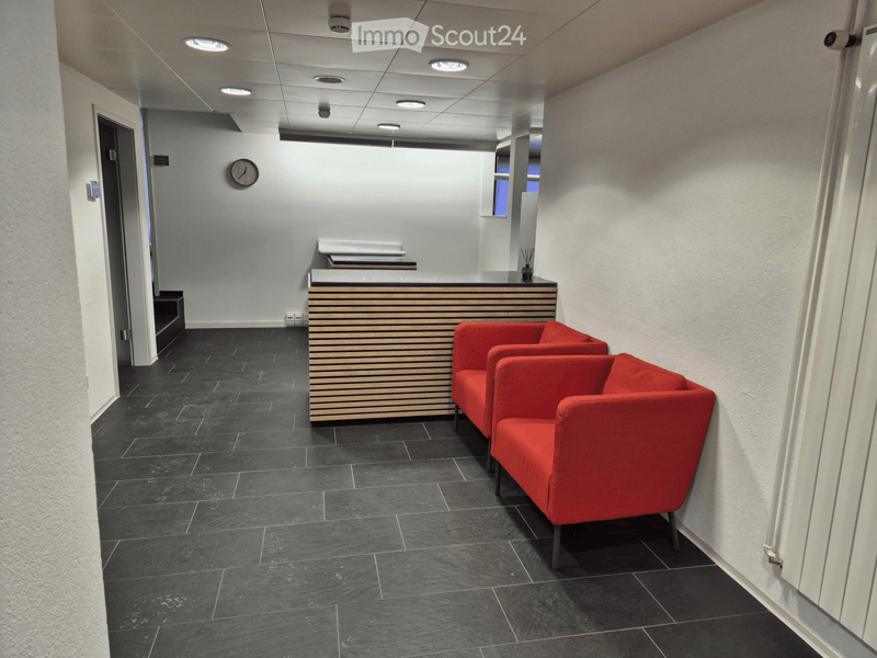 Modern reception area with dark tiled flooring, white walls, a reception desk, and red chairs.