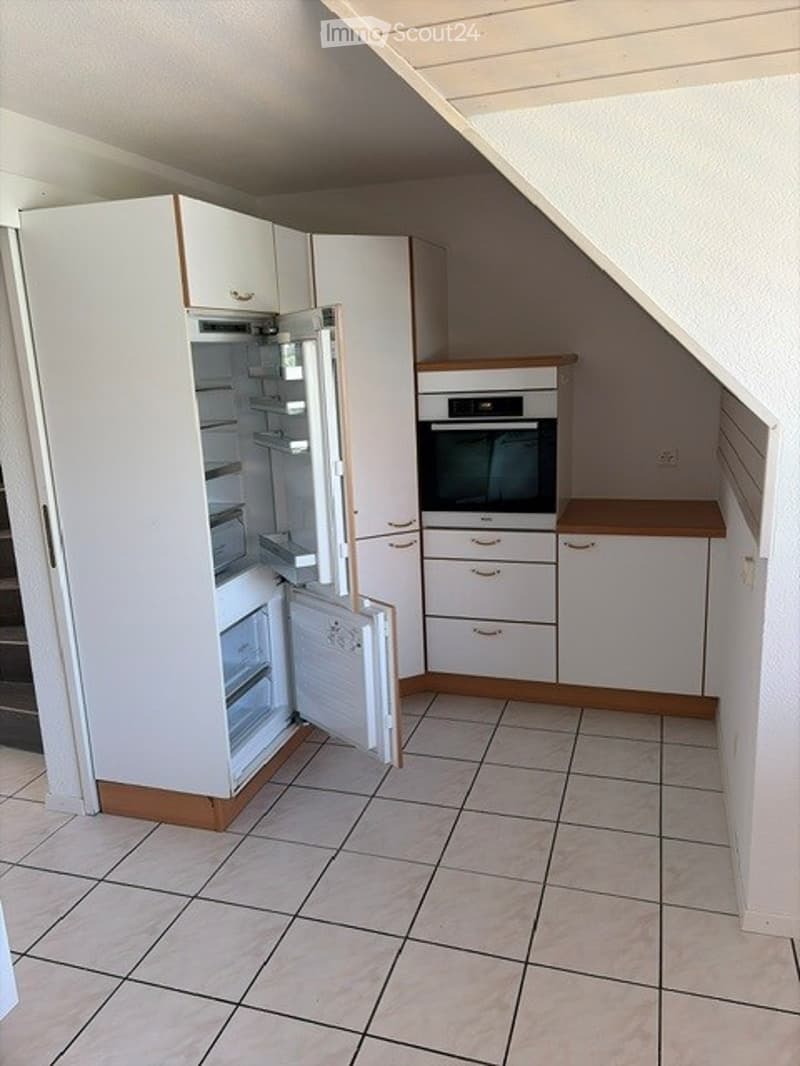 Modern kitchen with white cabinets, a refrigerator with open doors, and an oven. The floor is tiled, and the space features a wooden countertop.