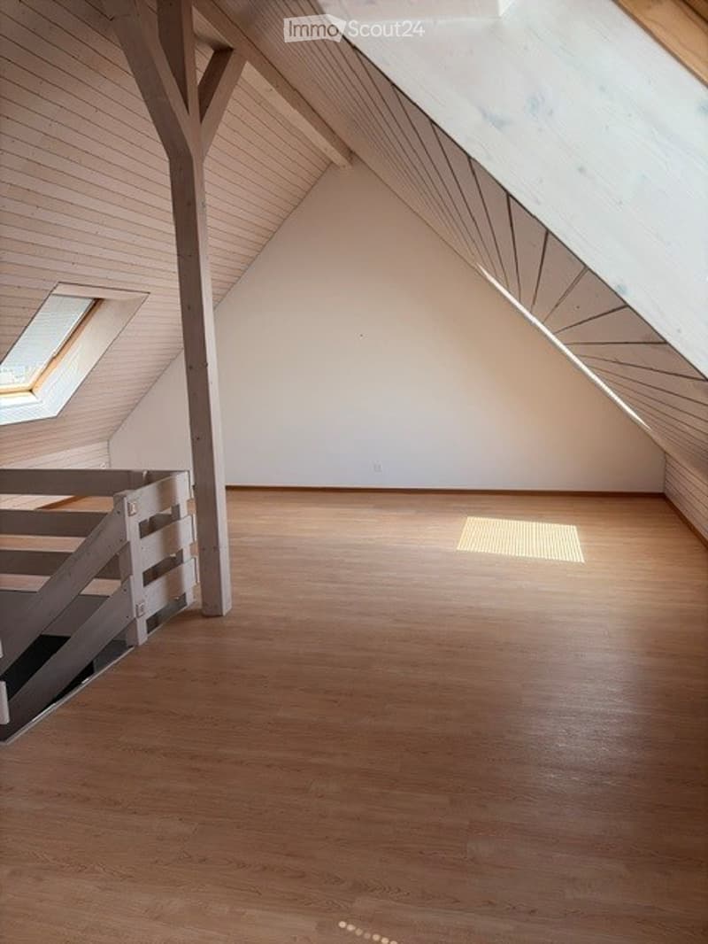 Empty attic room with wooden floors, white walls, and a skylight window allowing natural light to enter.