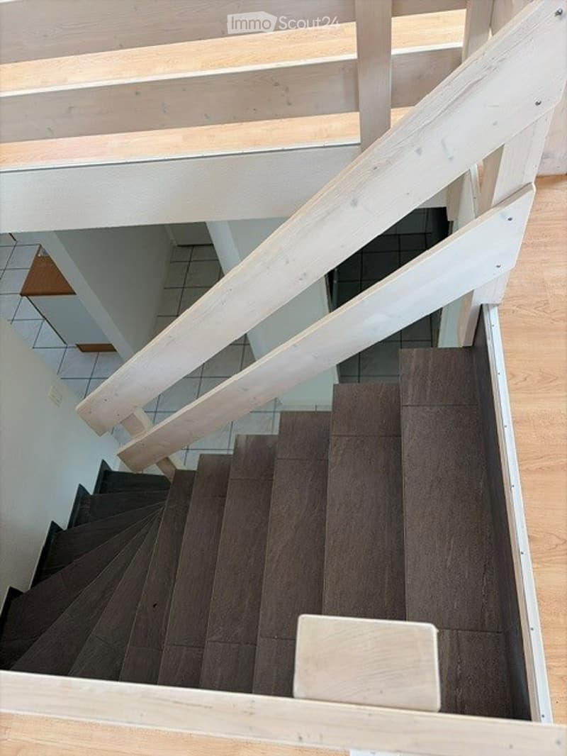 Spiral staircase with wooden steps and white railings, leading to an upper level with tiled flooring.