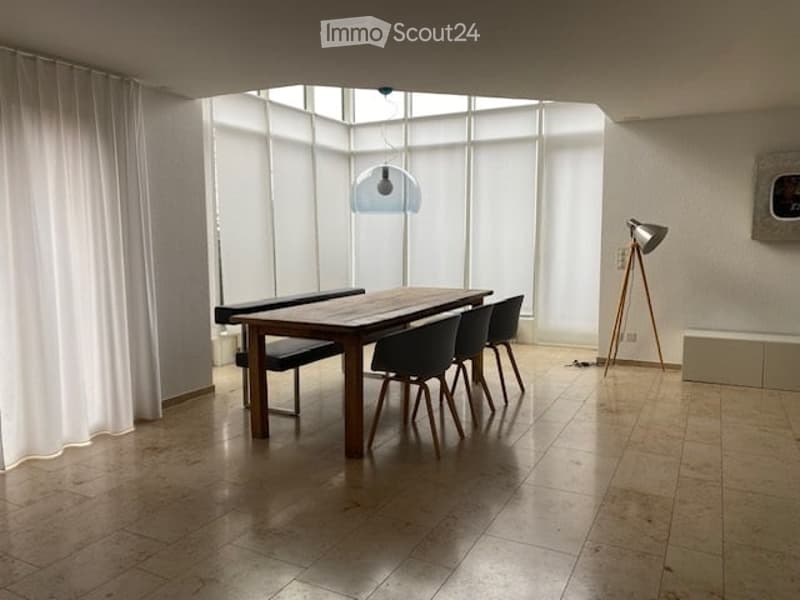 Dining area with wooden table and chairs, large windows, floor lamps, and white curtains.