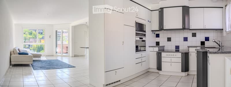 Modern, open-plan living and kitchen area with white cabinets, a sofa, a chair, a rug, and a sleek kitchen setup including an oven, microwave, and sink.