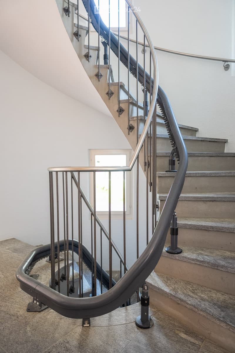 Spiral staircase with modern metal railing and beige stone steps, leading to an upper level.