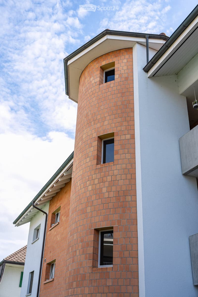 A modern residential building with a distinctive curved brick tower and multiple windows, featuring a combination of red brick and white walls.