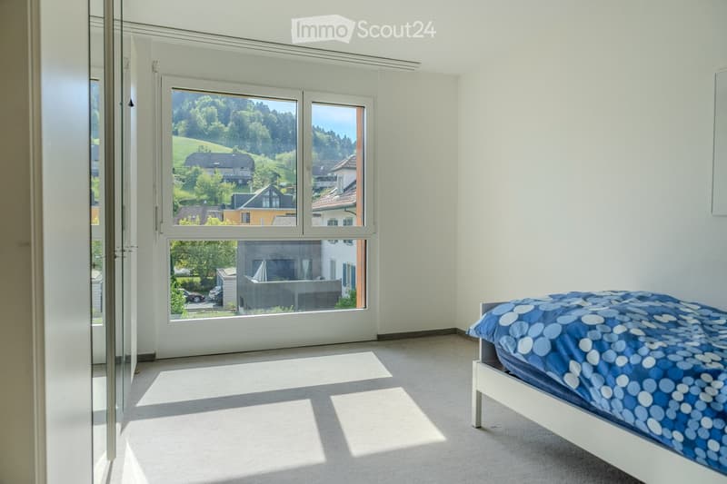 Bright bedroom with a single bed, large windows offering a scenic view of the surrounding landscape, and a glass door leading to an outdoor area.