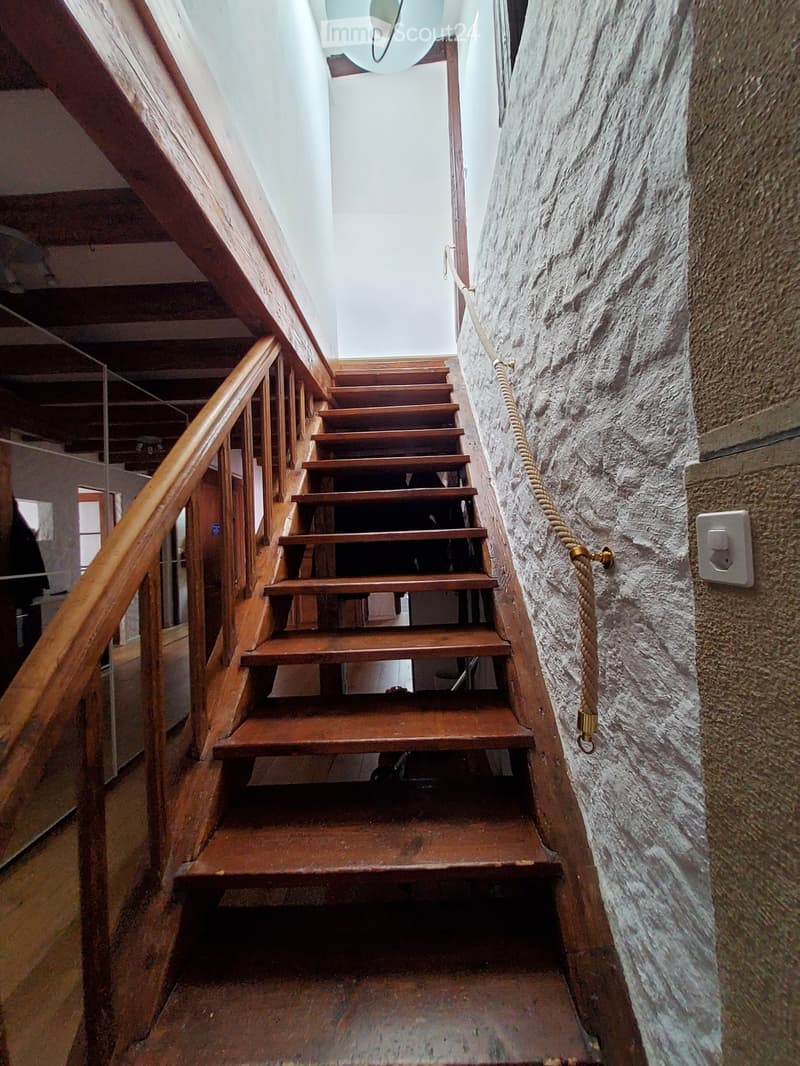 Wooden staircase with a handrail and rope side, stone wall, and visible light fixture at the top.