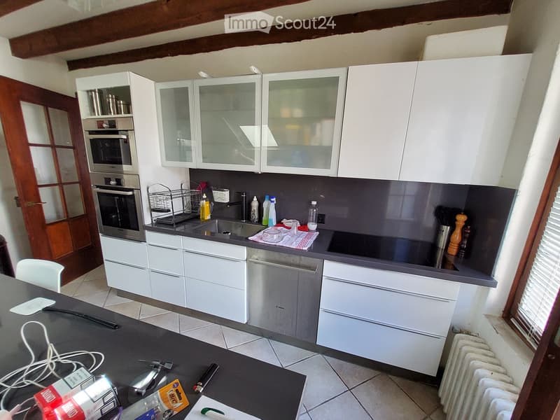 Modern kitchen with white cabinets, stainless steel appliances, and a dark countertop. Visible items include a sink, oven, dishwasher, and various kitchen utensils.