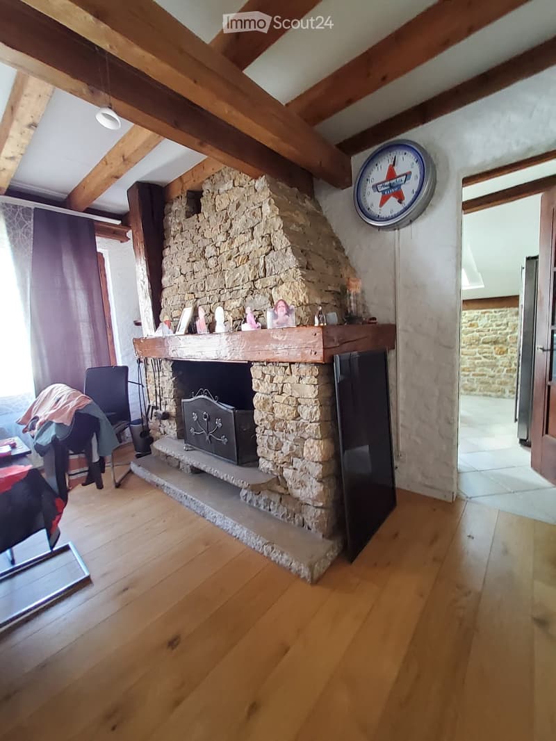 Living room with exposed wooden beams, stone fireplace, wooden floor, and a clock on the wall.