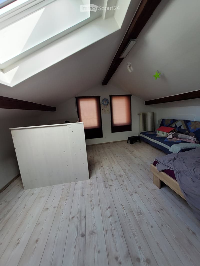 Attic bedroom with wooden flooring, slanted ceiling, skylight windows, and a small sofa bed.