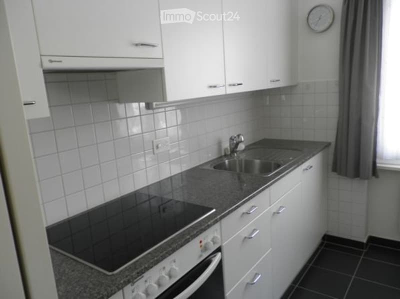 modern kitchen with white cabinets, black tiled floor, induction stove, stainless steel sink, faucet, dishwasher, clock on wall