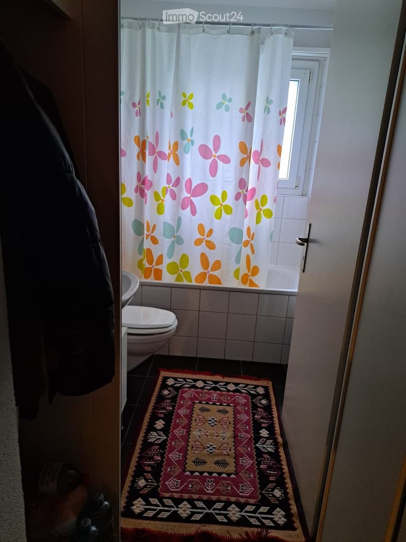 Bathroom with white tiles, white shower curtain, white toilet, white sink, rug, open door