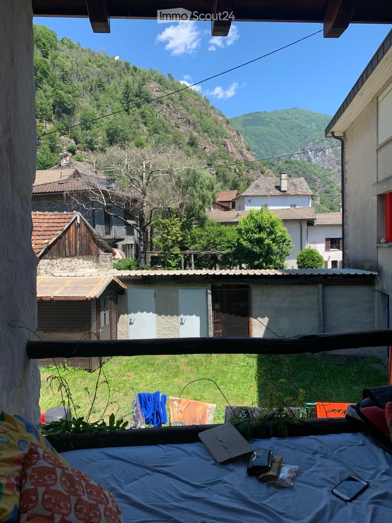 View from a balcony, showing a grassy yard with clothes hanging, a small shed, and a mountain in the background.