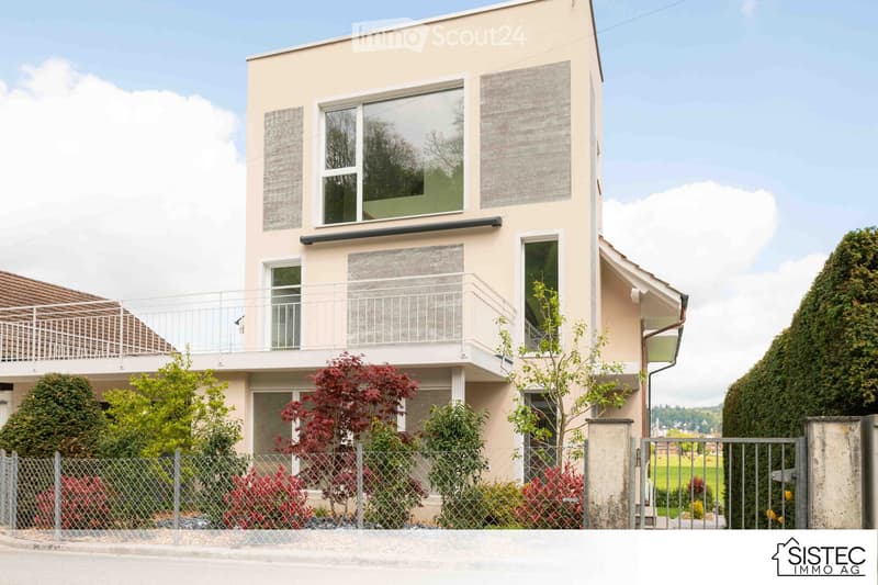 modern two-story house, beige facade, white windows, balcony, fenced garden, entrance gate