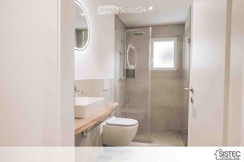 white walls, gray tiles, glass shower, white sink, round mirror, modern fixtures