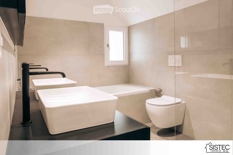 Bathroom with modern design, featuring beige tiles, large bathtub, modern toilet, white square sinks, and dark counters.
