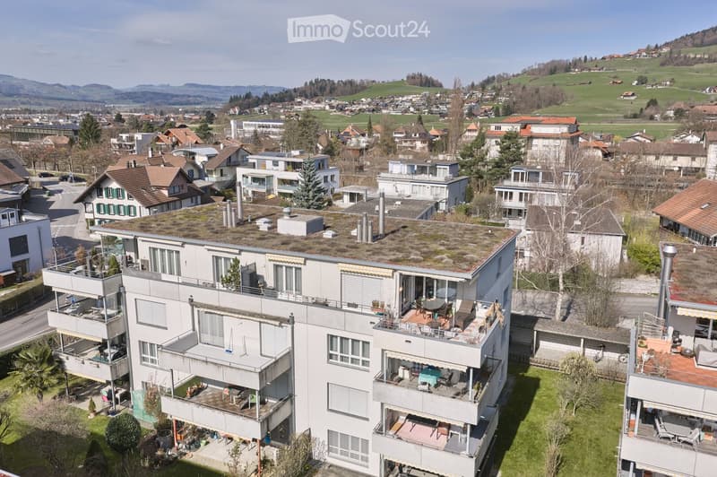 A multi-story residential building with multiple balconies and terraces, green roofs, and a green lawn in front.