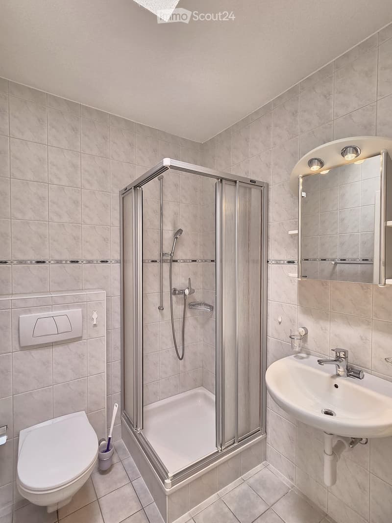modern bathroom with shower, toilet, sink, mirror, and tiled walls