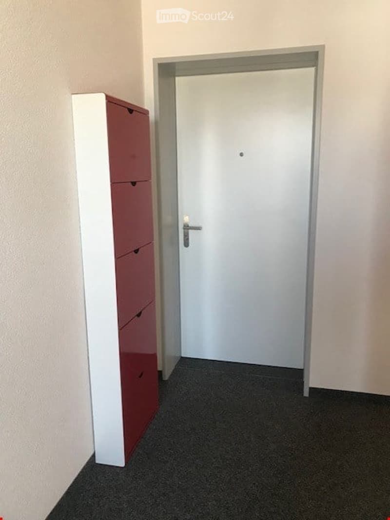 Empty room with a white door, a red and white cabinet, white walls, and a gray floor.