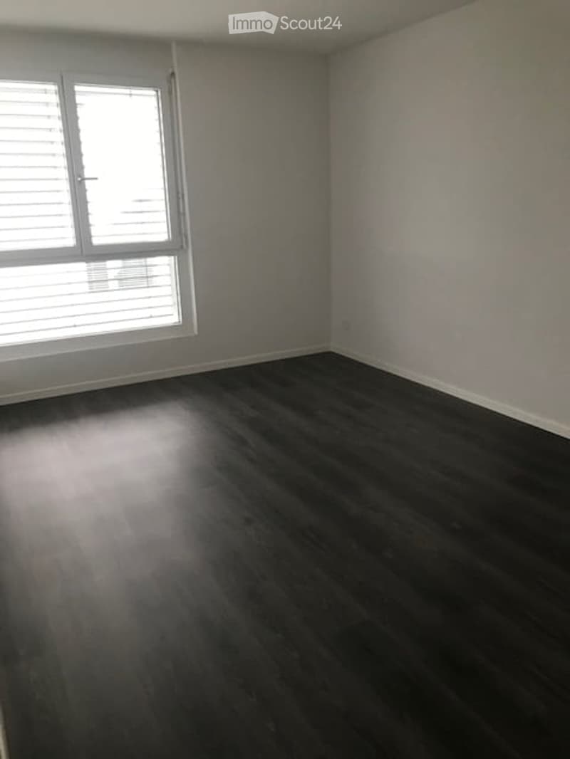 Unfurnished Room. Empty room with dark wooden flooring, white walls, and a large window with blinds.