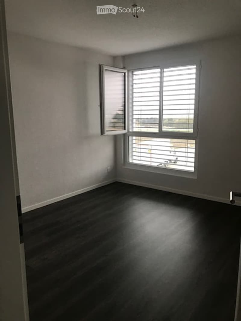 Unfurnished Room. Empty room with dark wooden flooring, white walls, and large windows with blinds. No furniture or equipment present.
