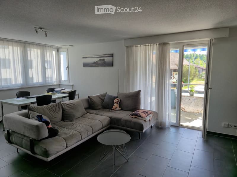 Furnished Room. Modern living room with a grey sectional sofa, small round table, dining table with chairs, and a view of the balcony.