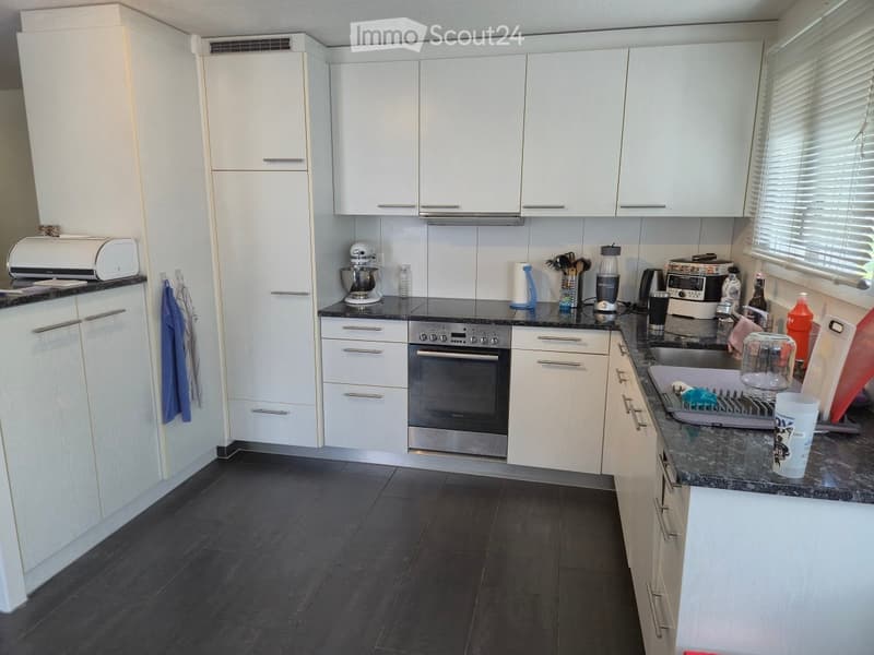Kitchen. Modern kitchen with white cabinets, dark countertops, and stainless steel appliances including an oven, blender, and toaster. The kitchen features a sink with a faucet, dish rack, and various kitchen utensils.