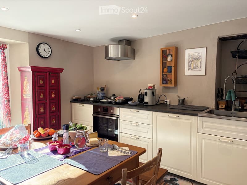 modern kitchen, wooden dining table, white cabinets, black counter, silver appliances, red cabinet, open door, fruits and vegetables, white curtains