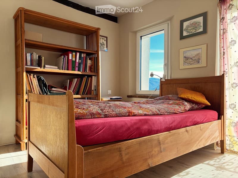 wooden bed, two pillows, two mattresses, wooden bookshelf, books, picture frames, lamp, window, natural light, hardwood floor