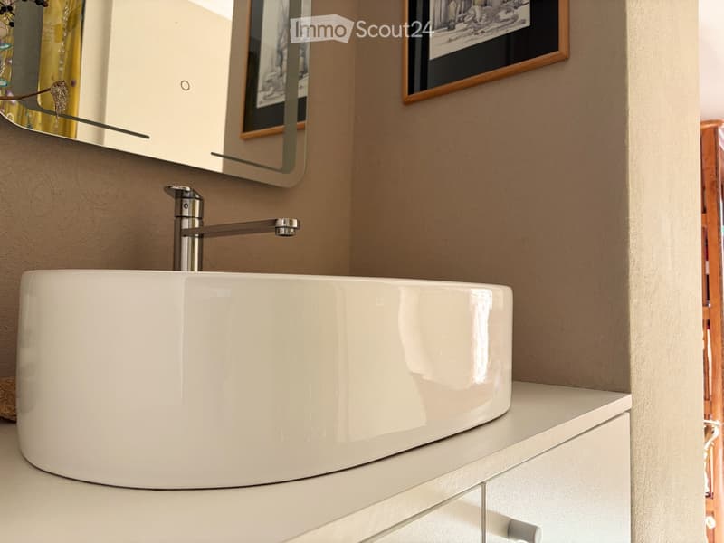 Modern bathroom, white basin, silver faucet, mirror, picture frame, white cabinetry, wooden door, tiled wall
