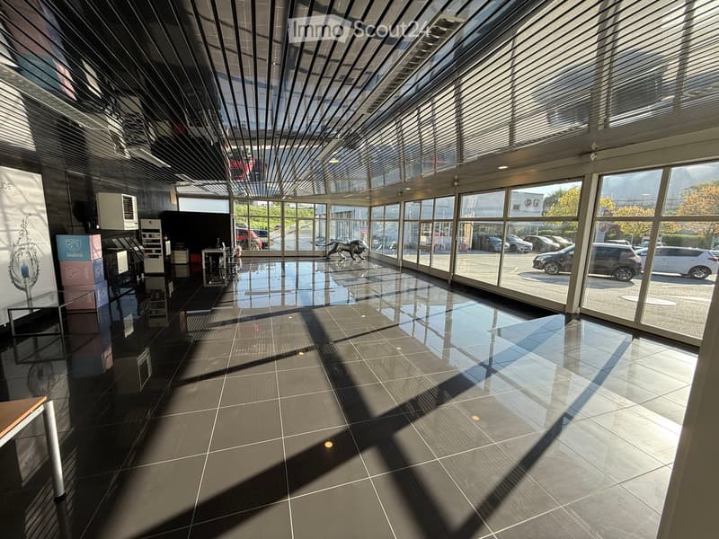 Furnished Room. Modern, spacious lobby with large glass windows, polished dark tiled floor, and a few pieces of furniture including a table, chair, and a screen.