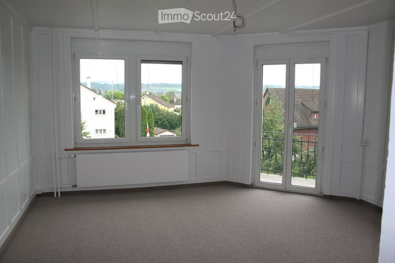 empty room, white walls, carpeted floor, large windows, balcony with railings, view of houses and trees