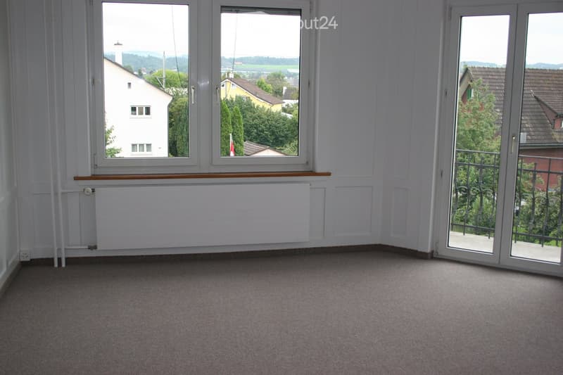empty room, white walls, carpeted floor, large windows, balcony with railings, view of houses and trees