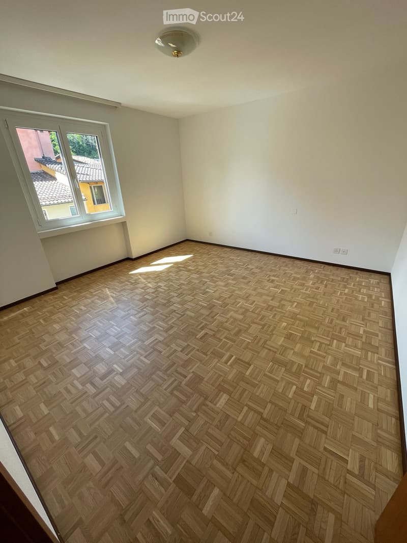 Unfurnished Room. Empty room with wooden herringbone flooring, white walls, and a large window with white frame. The room has a ceiling light fixture and visible electrical outlets.