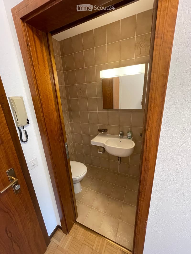 Bathroom. Small bathroom with beige tiled walls and floor, featuring a toilet, sink with a mirror above it, and a soap dispenser on the sink counter.
