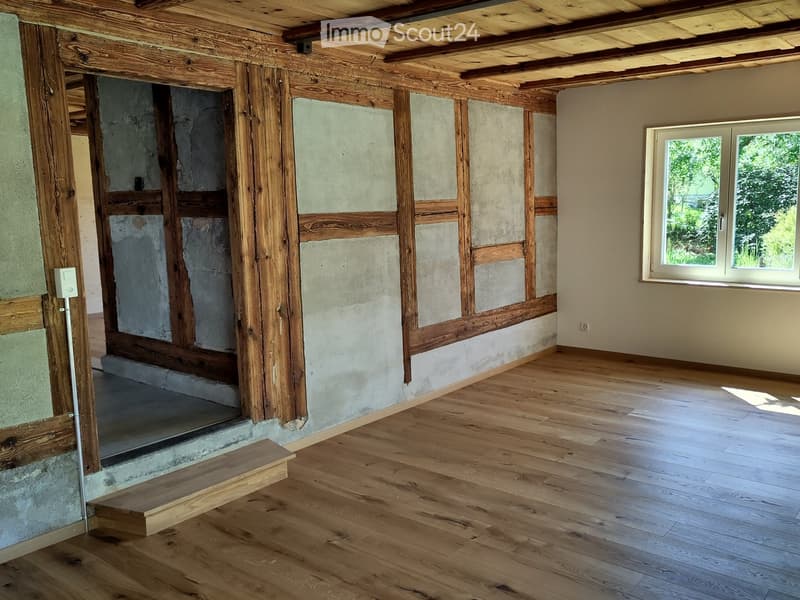 Unfurnished Room. An empty room with wooden beams, concrete walls, and wooden flooring. There is a window on the right side and a door on the left side.