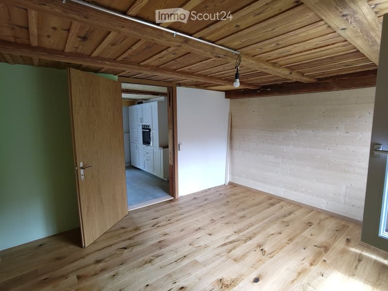 Unfurnished Room. Empty room with wooden floor and walls, open door leading to a kitchen.