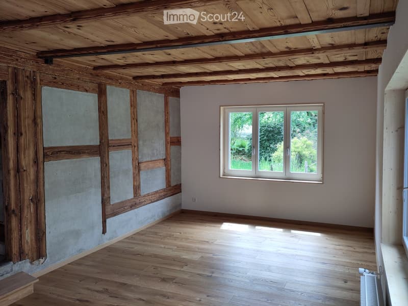 Unfurnished Room. Empty room with wooden ceiling, concrete walls, wooden beams, and wooden floor. A window with a view of trees outside.