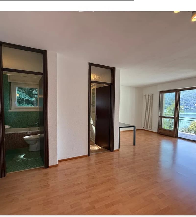 Unfurnished Room. Empty room with wooden flooring, large windows, and a view of the lake. Adjacent bathroom visible with a toilet and bathtub.