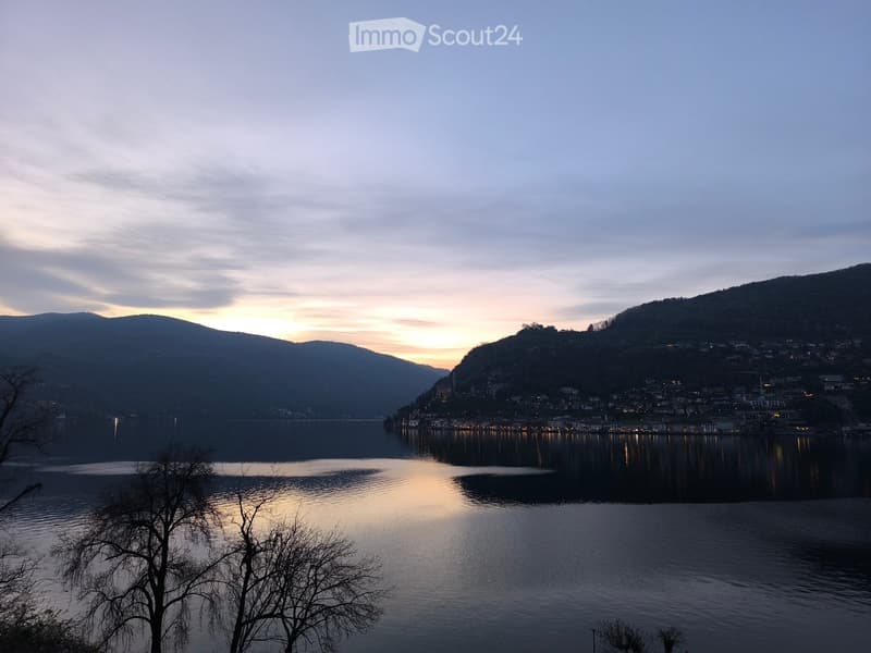 Garden / Outdoor Area. Scenic view of a lake at sunset with a town on the opposite shore, surrounded by hills and mountains.