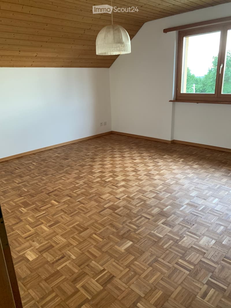 Unfurnished Room. Empty room with wooden herringbone flooring, white walls, and a large window with a view of greenery. A hanging pendant light is visible.