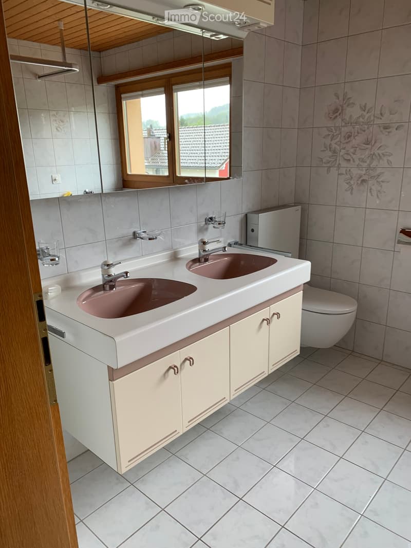 Bathroom. Bathroom with double sink, mirror, toilet, and cabinets. Light-colored tiles and wooden accents.