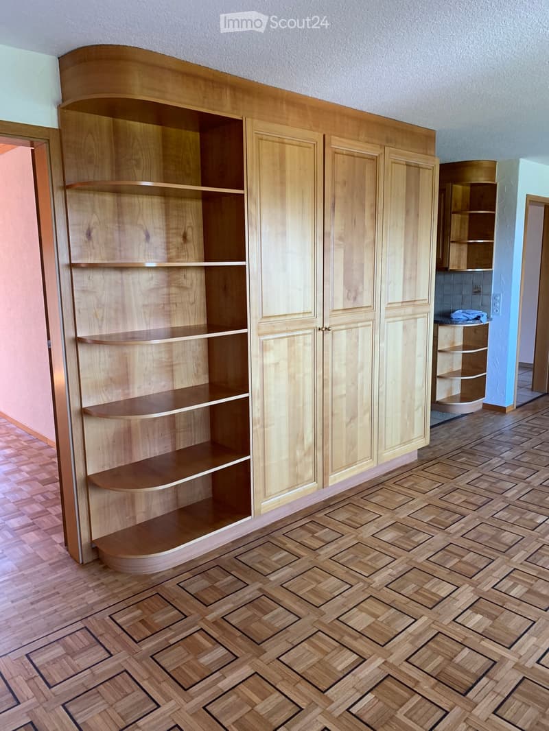Unfurnished Room. Empty room with wooden herringbone flooring and built-in wooden shelving unit with open compartments and closed cabinets.