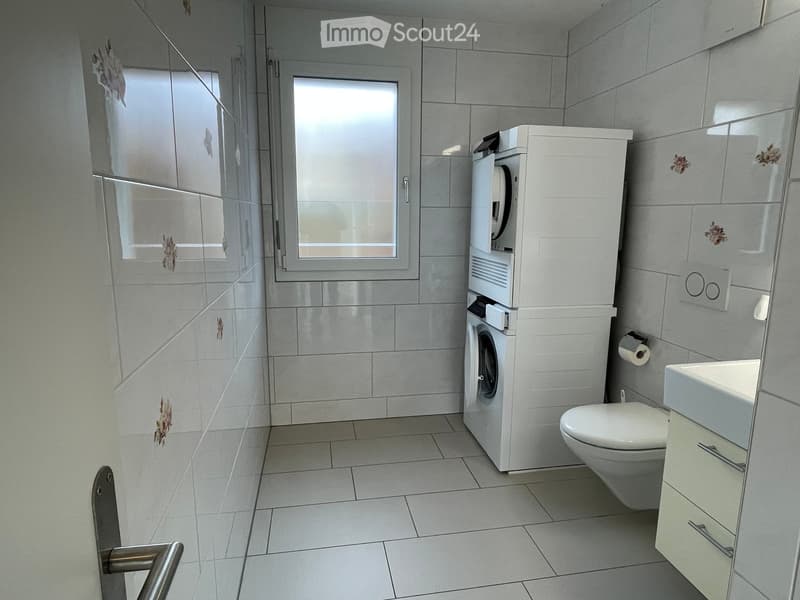 Small laundry room with washing machine, dryer, white tiled walls, white tiled floor, white toilet, and sink